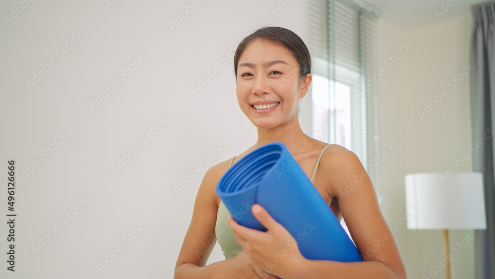 Close up of happy pretty woman wearing sportswoman bra holding yoga mat standing in the living room and smile. Healthy and active lifestyle. Refreshing after yoga practice. Exercise concept Close up of happy pretty woman wearing sportswoman bra holding yoga mat standing in the living room and smile. Healthy and active lifestyle. Refreshing after yoga practice. Exercise concept