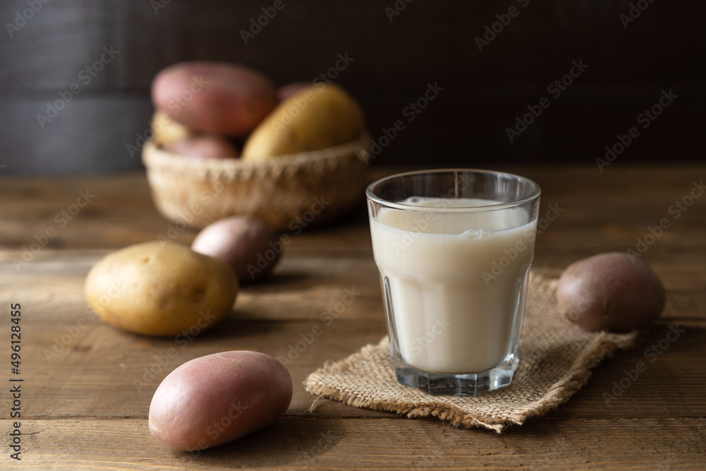 Vegan potato milk in glass and milk jar with raw potatoes on the wooden background in rustic style Vegan potato milk in glass and milk jar with raw potatoes on the wooden background in rustic style