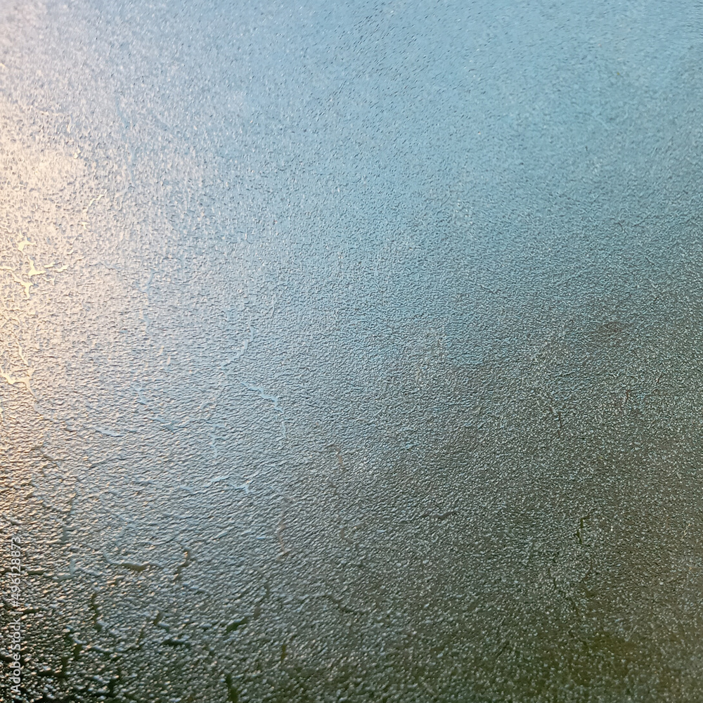 Background, texture. Frozen glass with the onset of cold weather. View through the ice layer of the blue sky.