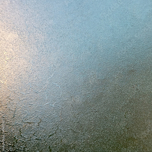 Background, texture. Frozen glass with the onset of cold weather. View through the ice layer of the blue sky.