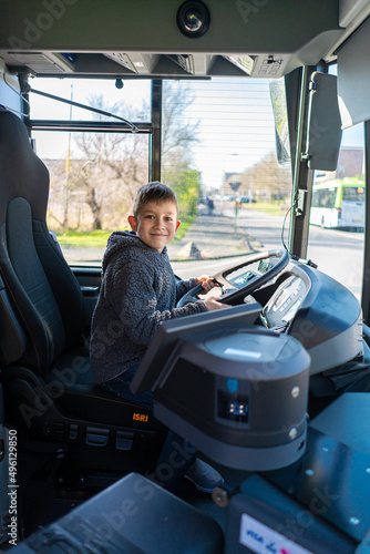 A boy drive a bus. The boy turns the steering wheel in the abandoned bus. The boy is playing on the bus