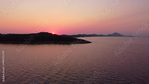 flying up, revealing colourful sunset above an island with vegetation and hills photo