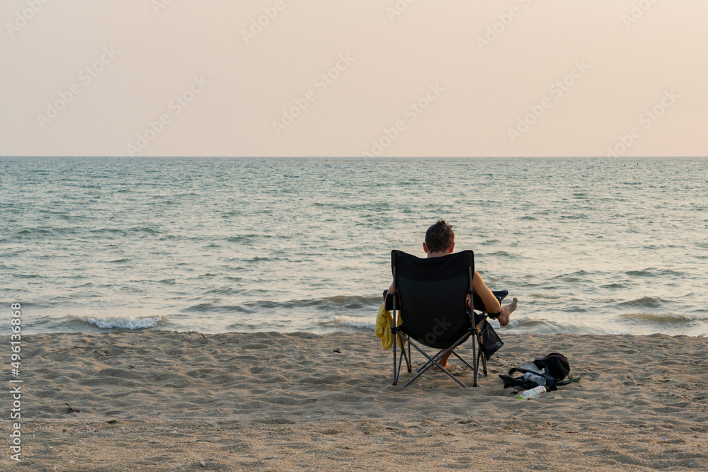 A man sits in a chair on the beach during sunset.