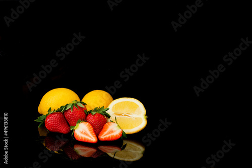 Dojrzałe truskawki i cytryny na czarnym tle, całe i przekrojone photo