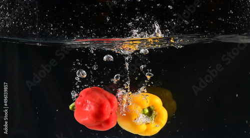 Close up of The red, yellow and green bell peppers fell into the water and the water splashed up with black background. Concept for health and vitamins.