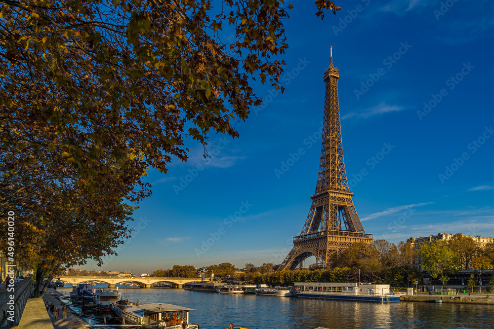Fototapeta premium Eiffel Tower Enlightened by Sun at Day in Paris Fall Colors Trees Seine River and Boat Cruises