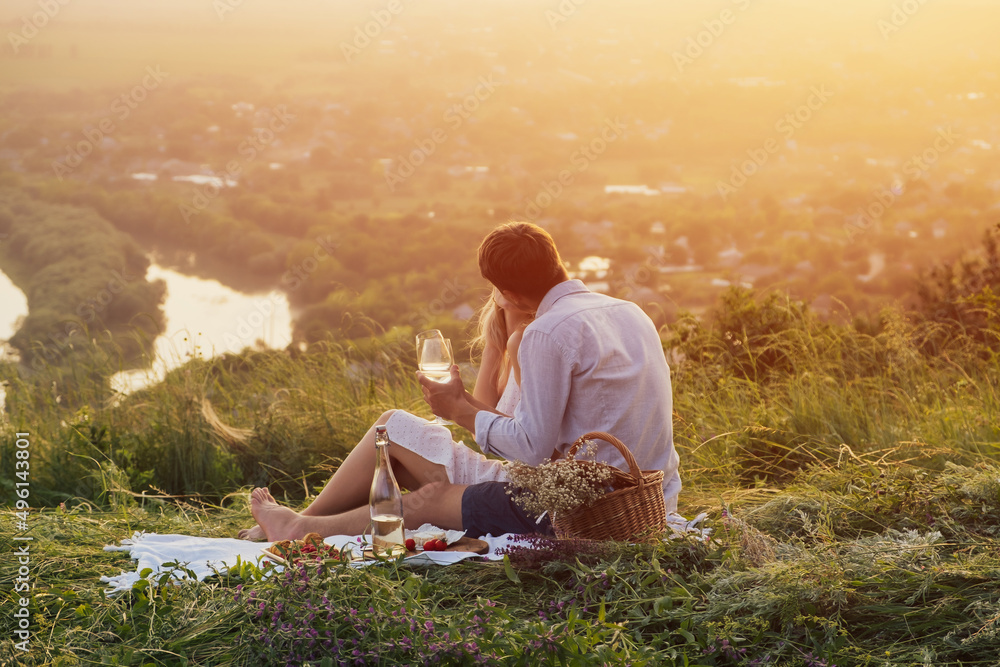 Young couple sitting on picnic while spending time together on the hill. Romantic atmosphere at sunset.
