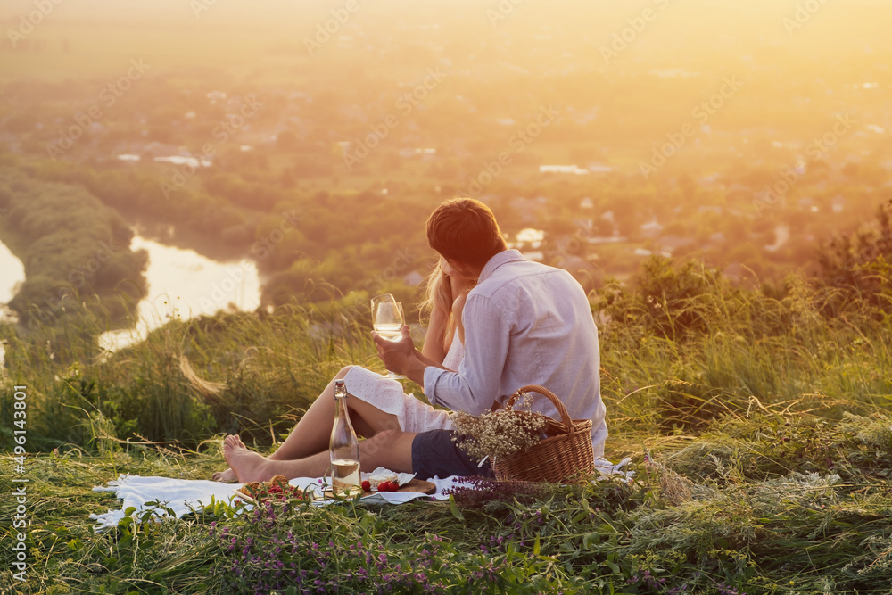 Young couple sitting on picnic while spending time together on the hill. Romantic atmosphere at sunset. Young couple sitting on picnic while spending time together on the hill. Romantic atmosphere at sunset.