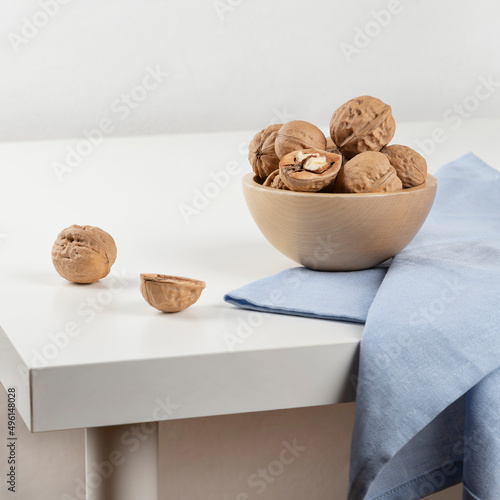 There is a wooden bowl with walnuts on a white table, and a blue towel is lying next to it. Close-up. photo