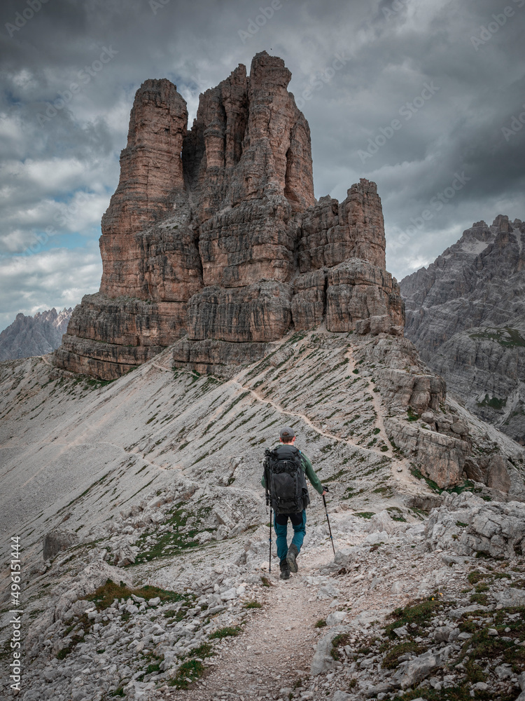 Man with backpack hiking with view to Sasso di Sesto mountains peak in the Dolomite Alps in South Tyrol with dramatic dark sky, Three Peaks Nature Reserve, Italy.