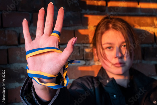Angry girl stands on the wall background of her ruined house with a flag of ukraine on her palm. Stop War. Peace in Ukraine.  No war, stay with Ukraine. Protest. Selective focus