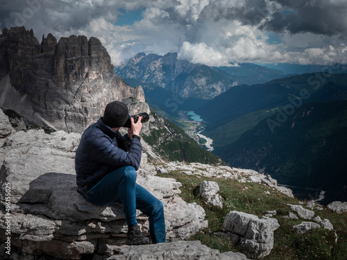 Man taking photos with camera with view to mountain summits in the Dolomite Alps in South Tyrol with clouds in sky, Three Peaks Nature Reserve, Italy.