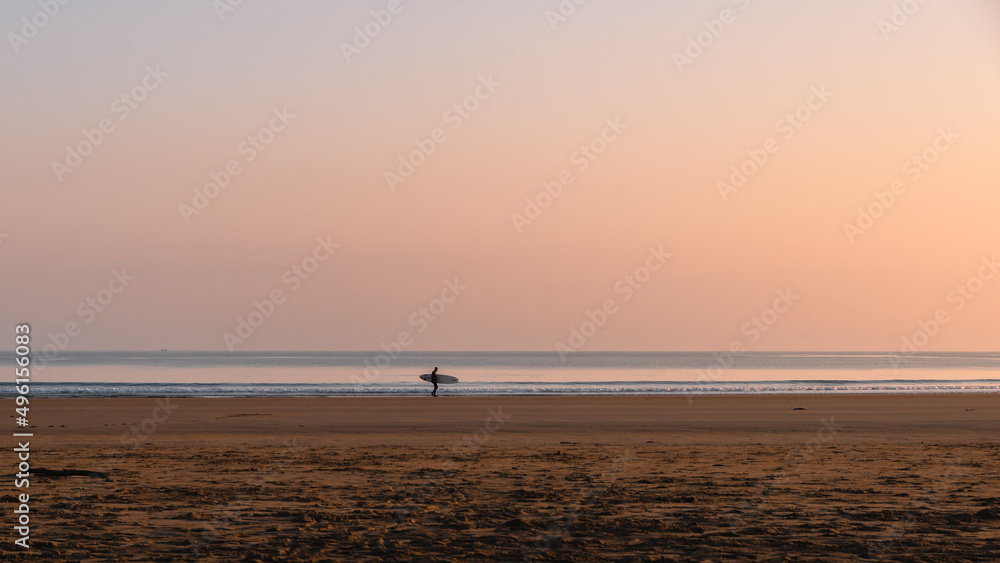 The pastel pinks and blues glow above a lone surfer at the water's edge on Belhaven Bay to the south of the North Sea
