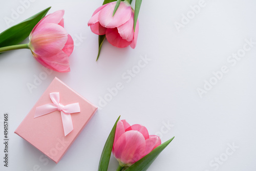top view of gift box near bright pink flowers on white.