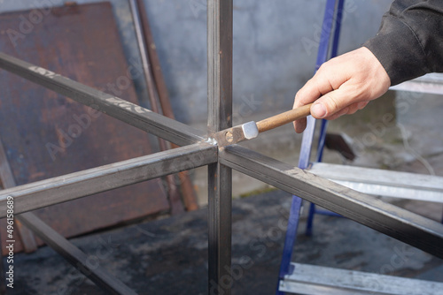 a man with a hammer beats scales when welding on an iron structure