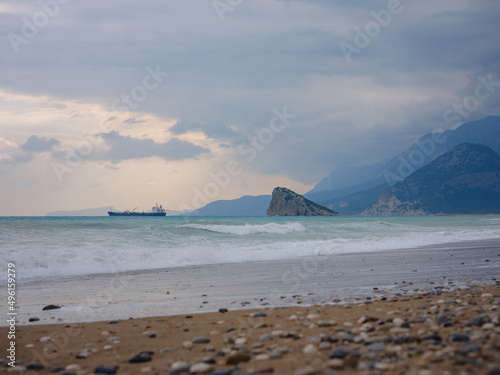 Cargo ship in calm blue Mediterranean in Anatalya. Traveling along the Mediterranean Sea, view of rocky coast of Antalya. In distance, cargo ships are visible. photo