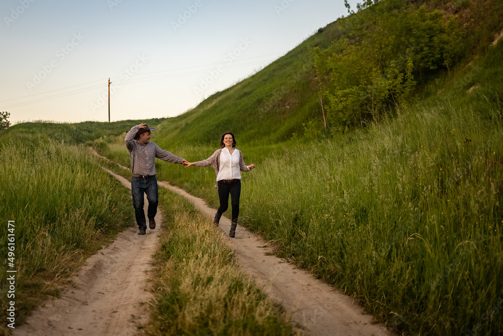 a couple in love runs holding hands along the road in the village. Guy in a cowboy hat