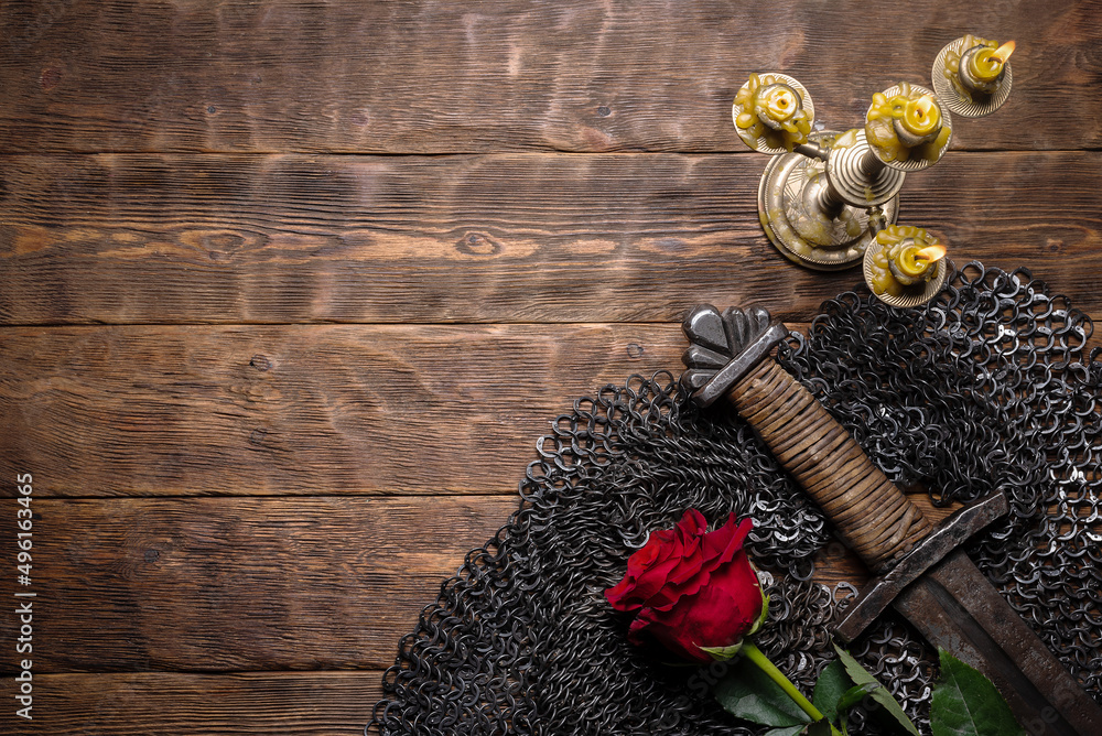 Knight sword and red rose flower on the black woorden flat lay table background with copy space. Knight sword and red rose flower on the black woorden flat lay table background with copy space.