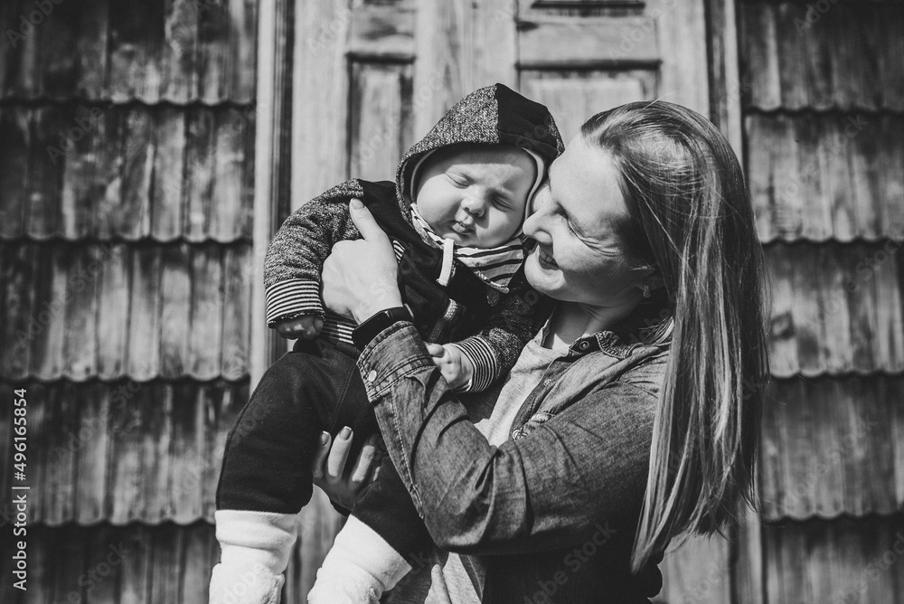 Young mother with son. Happy mom hugs baby in nature on the background of an old wooden architectural house. Black and white photo.