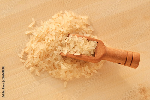 Rice scattering in a wooden spoon on a light board. The product is dietary, the benefits of proper nutrition. Cereals in nutrition - concept.