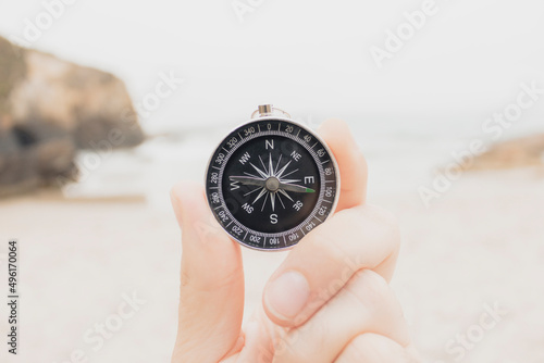 Closeup, hand holding an analog compass on the beach in front of the sea, concept travel, summer, selective focus.