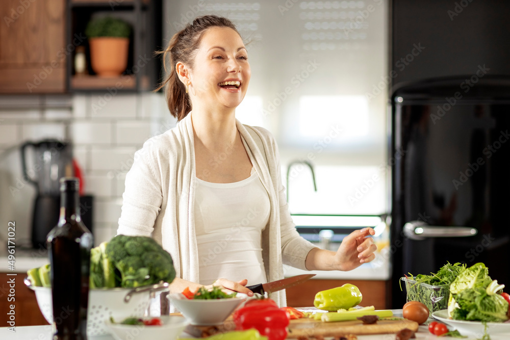 Pregnant woman in the kitchen preparing healthy vegetarian food and smile