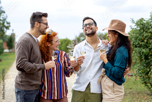 Four friends standing in vineyard with glasses of vine red and white drinking, relaxing and talk to each other in summer day.