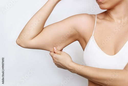 Close-up of a young caucasian woman grabbing skin on her upper arm with excess fat isolated on a white background. Pinching the loose and saggy muscles. Overweight  liposuction concept