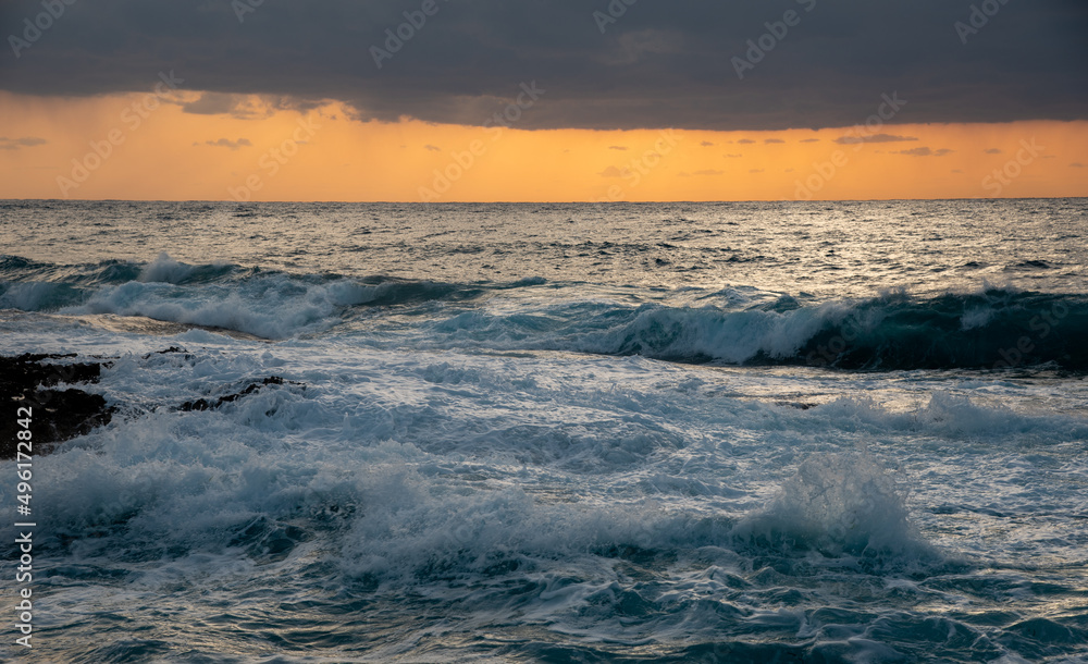 Obraz premium Windy waves splashing on the rocky coast at sunset. Stormy sky in winter