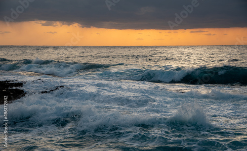 Windy waves splashing on the rocky coast at sunset. Stormy sky in winter