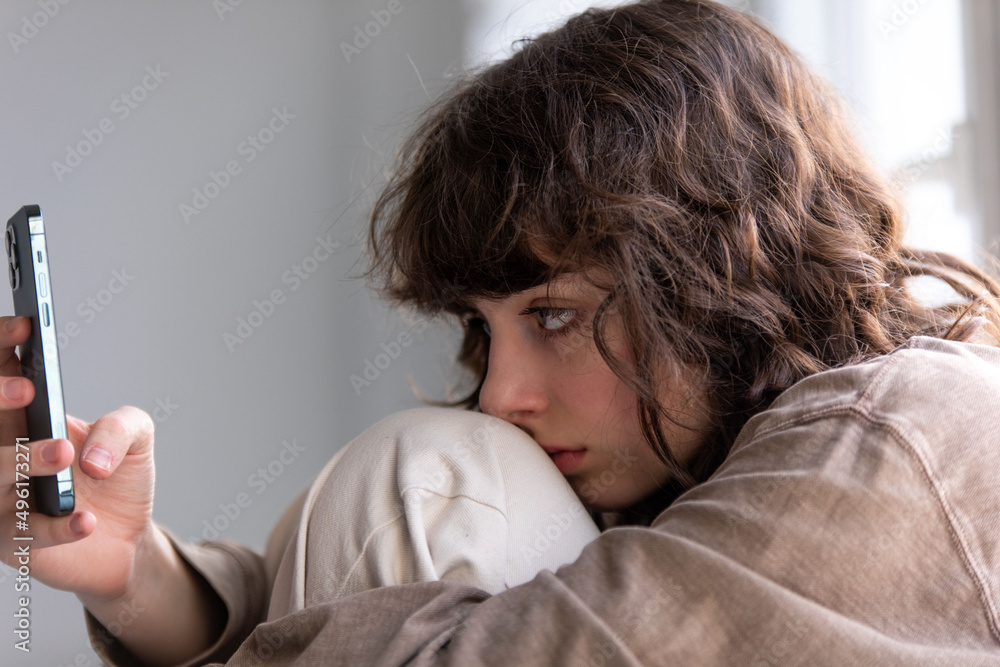 Portrait of a curly girl using a smartphone while sitting by the window. Portrait of a curly girl using a smartphone while sitting by the window.