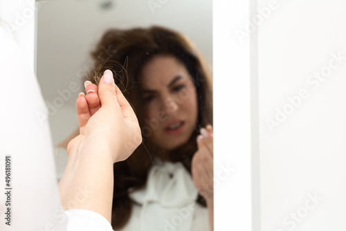 Young girl suffering from trichotillomania in the mirror looking at a lock of hair between her fingers photo