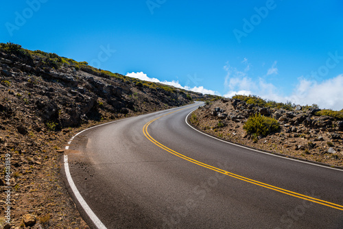 Fotografía A road curves though a rocky landscape above clouds into a bright blue sky - Hal