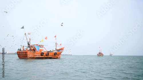 Sea gulls flying over Boats in the Arabian sea at Okha Port in Gujarat, India. Fishing boats at the port with Indian flag on top of them. Small wooden fishing boats in the arabian sea.  photo