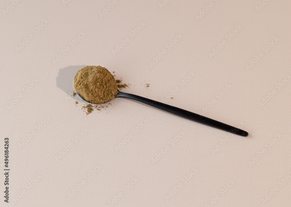 A spoon with hemp flour lies on a beige surface. Top view. A spoon with hemp flour lies on a beige surface. Top view.