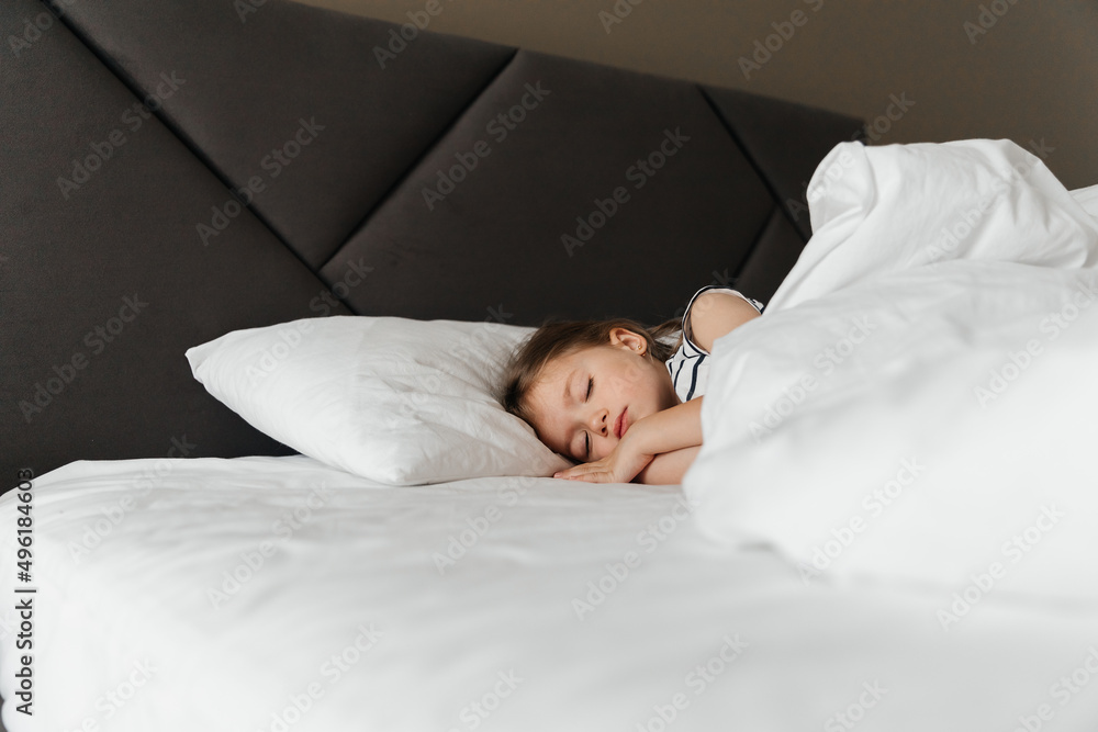 The little girl went to bed for a nap in her parents' bed. Portrait of a girl falling asleep in bed during the day The little girl went to bed for a nap in her parents' bed. Portrait of a girl falling asleep in bed during the day