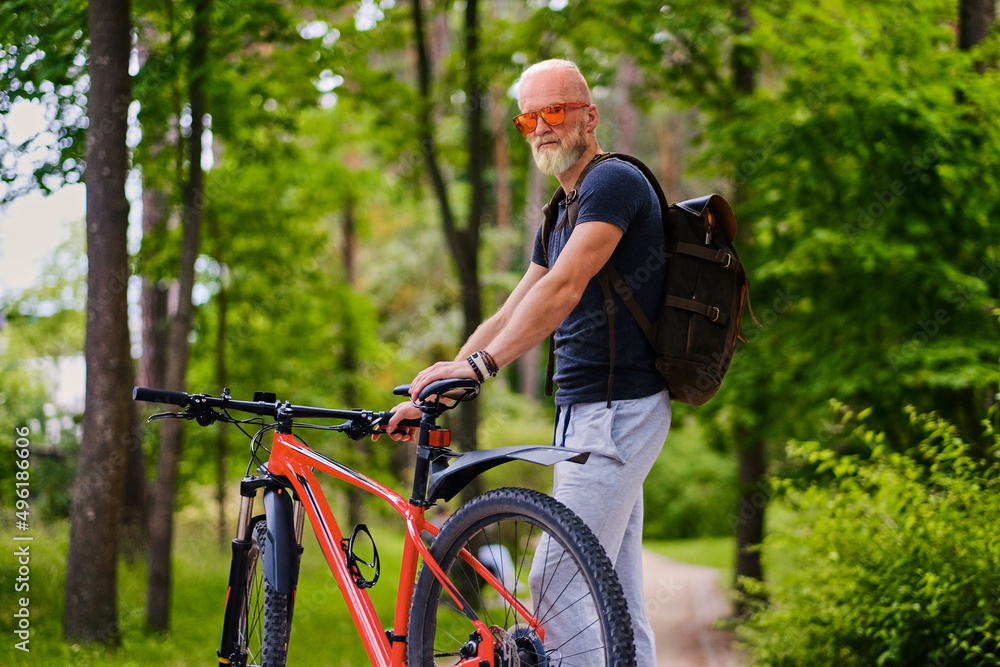 Sportive aged man bicyclist with bicycle and backpack outdoors