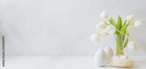 White spring tulips in a vase, easter eggs on a white table. Mock up for displaying works