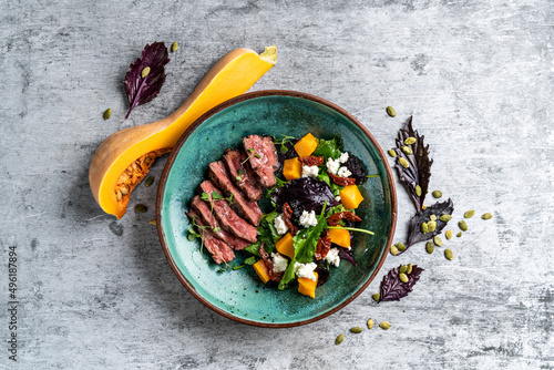 фотографія Baked pumpkin salad, spinach, tomato and beef in a white plate on a stone backgr