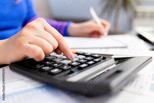 Woman using calculator for calculate domestic bills at home, doing paperwork for paying taxes photo