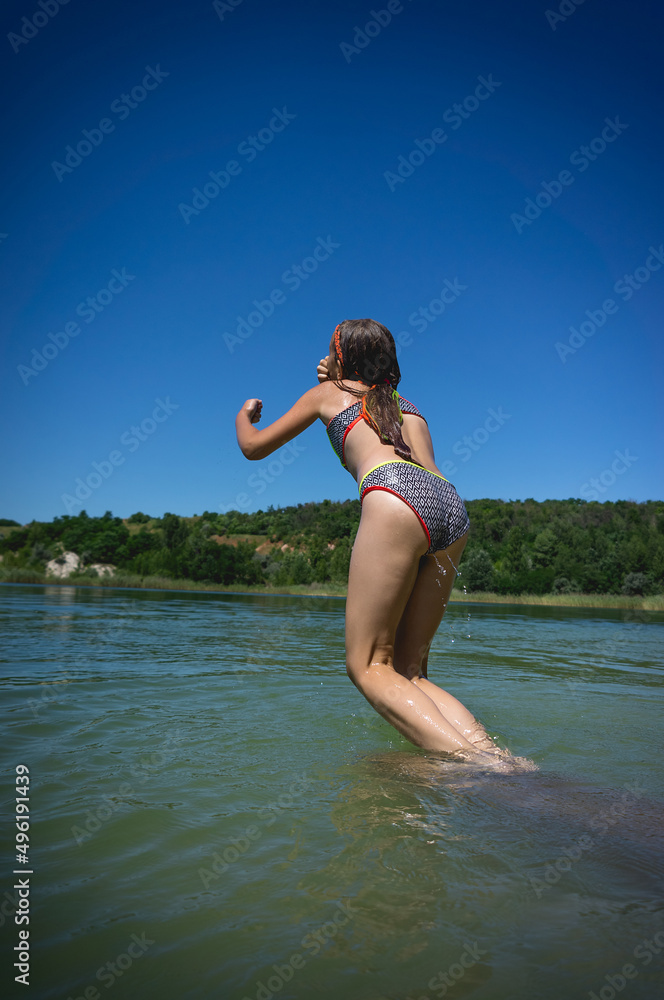 Naklejka premium A little cute girl in a swimsuit jumps into the blue water of a career lake.