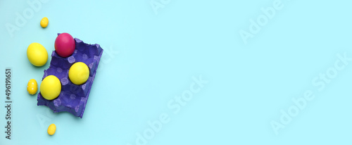 Holder with painted Easter eggs on light blue background with space for text