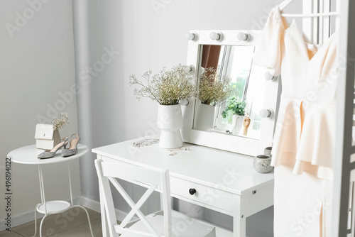 Photo Vase with gypsophila flowers and jewelry on dressing table near light wall