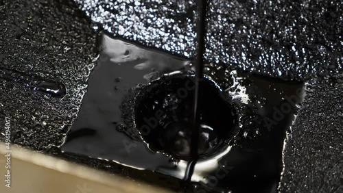 BLACK CRUDE OIL is pouring into a metallic container for lab analysis. Close-up shot emphasizes the density and viscosity of fossil fuel in an industrial setting.