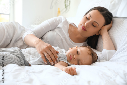 Beautiful young mother lying with her sleeping baby on bed