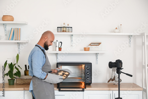 Young man putting raw peach muffins into oven in kitchen