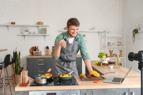 Young man sprinkling spices onto vegetables while recording video in kitchen