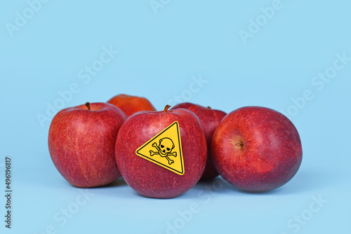 Red apples with poison skull symbol sticker on blue background. Concept of pesticide residues in agricultural food photo