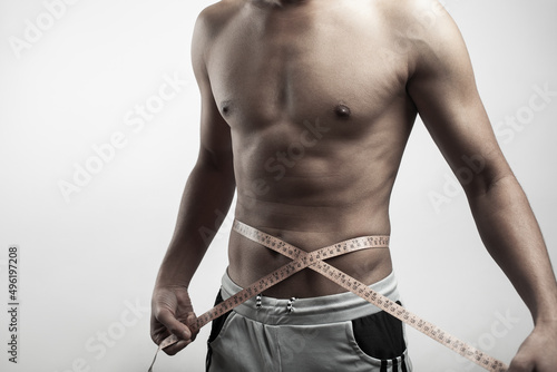 male muscular fitness model torso with measuring tape around his six pack belly