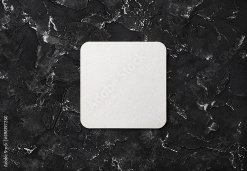 Blank square beer coaster on black plaster background. Flat lay.